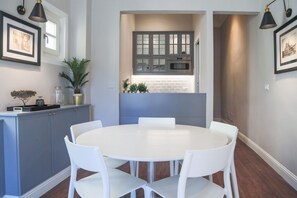 Une cuisine moderne avec des meubles gris, un plan de travail blanc et une table de salle à manger ronde, assortie de chaises blanches.