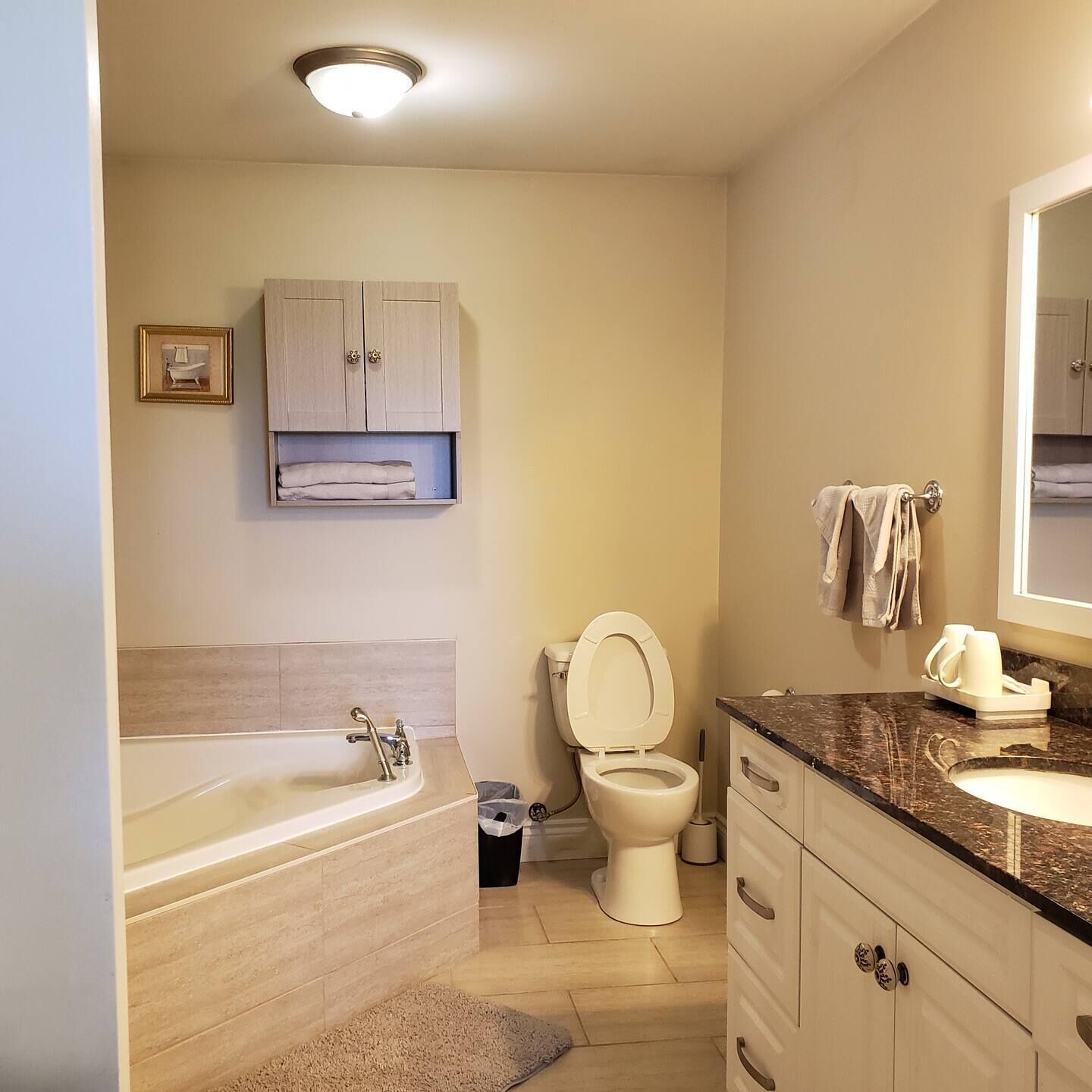 Un baño con bañera, inodoro, lavabo y un armario sobre el inodoro.
