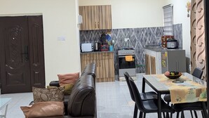 A modern kitchen with a built-in oven and microwave, a dining area with a table and chairs, and a brown leather sofa with cushions. - Emaric Homes (Accra)