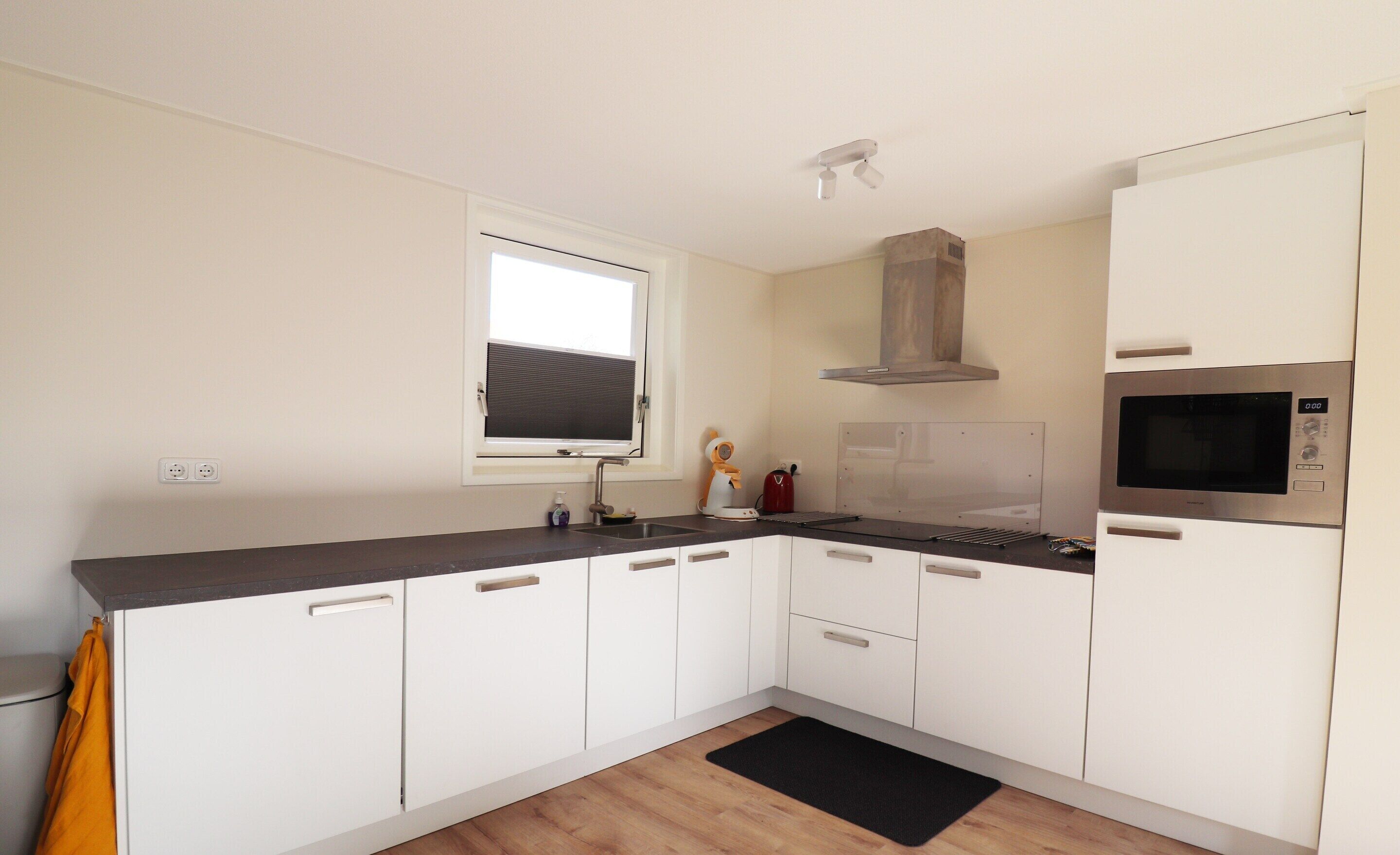 A modern kitchen with white cabinets, a built-in microwave, and a window above the sink.