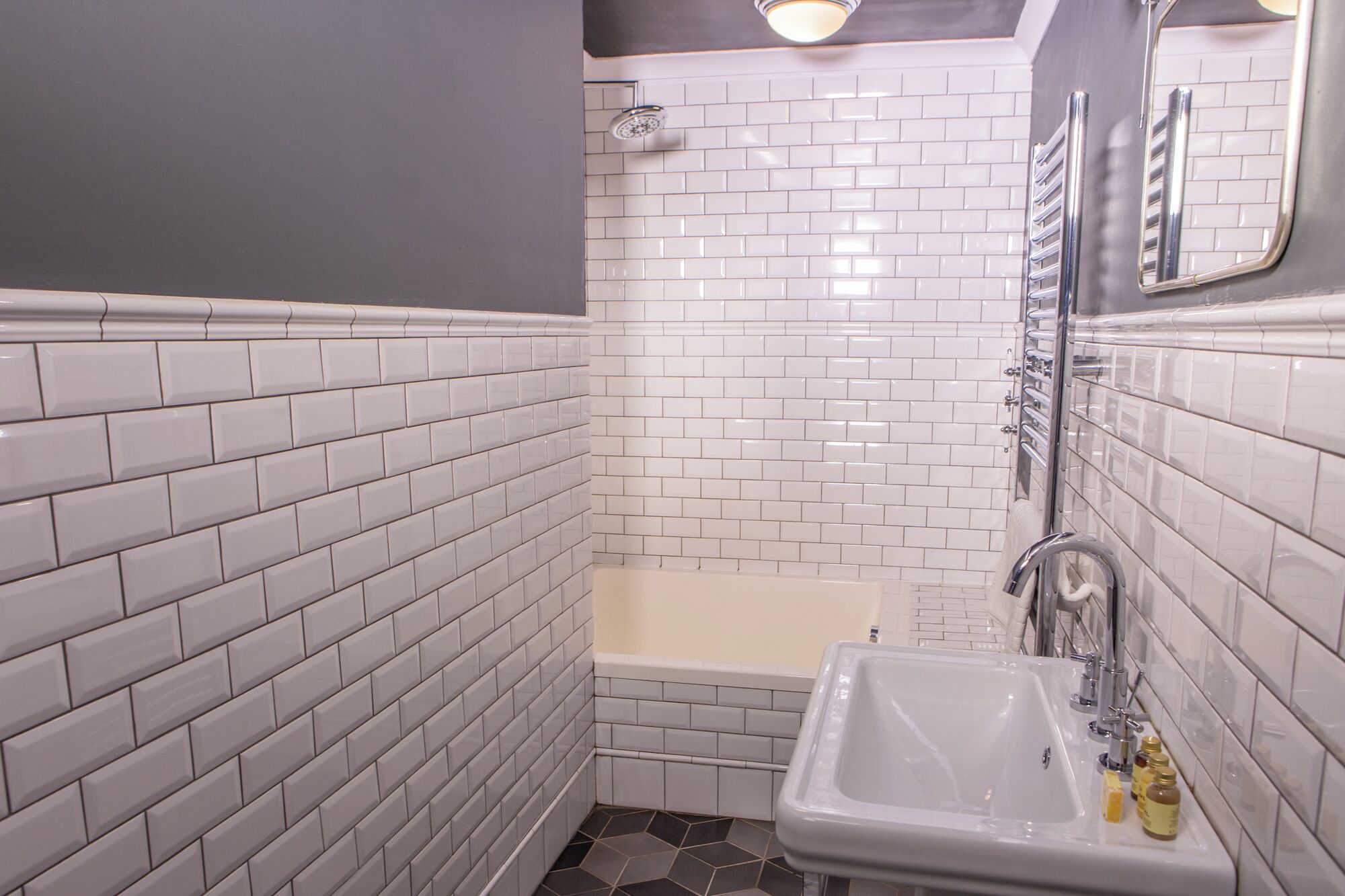 A bathroom with white subway tiles, a bathtub, a sink with toiletries, and a shower.