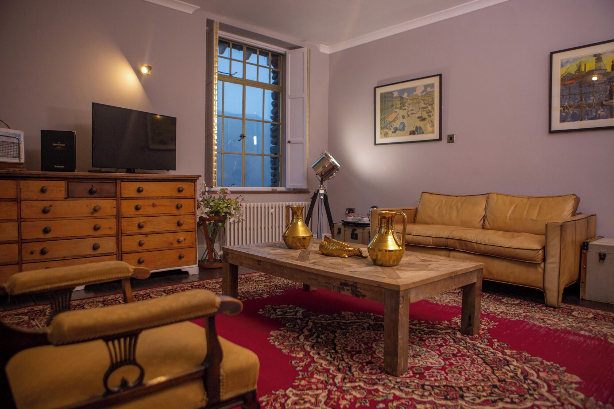A living room with a sofa, armchairs, a wooden coffee table, and a red patterned carpet.