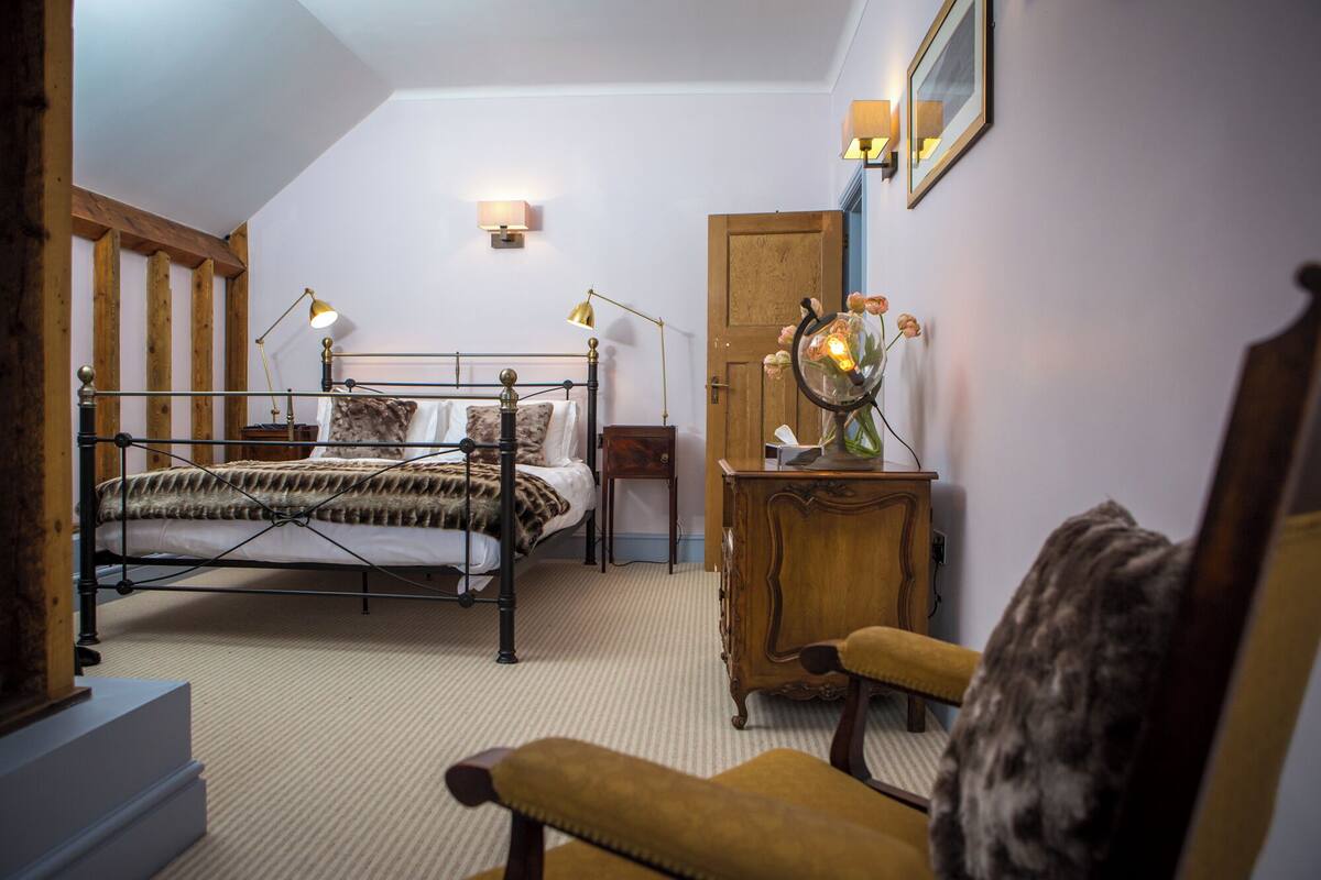 A bedroom with a metal bed frame, a wooden dresser, a chair, and a desk with a lamp.