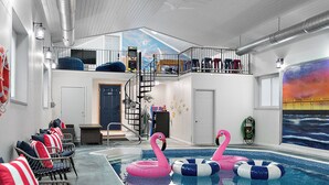 Una piscina interior con dos flamencos rosados, una escalera y un mural de un atardecer.