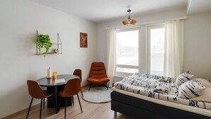 A modern, well-lit room with a dining table, chairs, a sofa, and a large window with curtains.