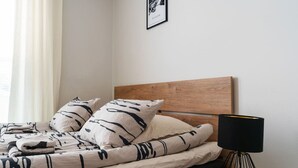 A neatly made bed with a wooden headboard, a black lamp on a side table, and a framed picture on the wall.