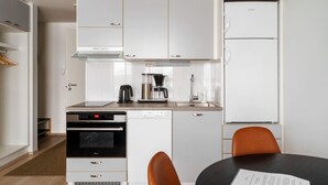 A compact kitchen with a built-in oven, dishwasher, and coffee maker. There is a dining table with two chairs and a small refrigerator.