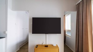 Habitació d'hotel amb televisió de pantalla plana penjada a la paret, taula de nit de fusta amb un comandament a distància, un objecte decoratiu petit i una finestra amb cortines.
