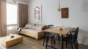 Un saló modern amb un sofà, taula de dinar i cadires. Hi ha un finestral amb cortines, una làmpada de paret i un quadre encimbellat.