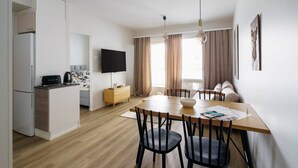 Una cuina moderna amb forn integrat, zona de menjador amb taula i cadires de fusta, televisió de pantalla plana i sofà a la zona de estar.
