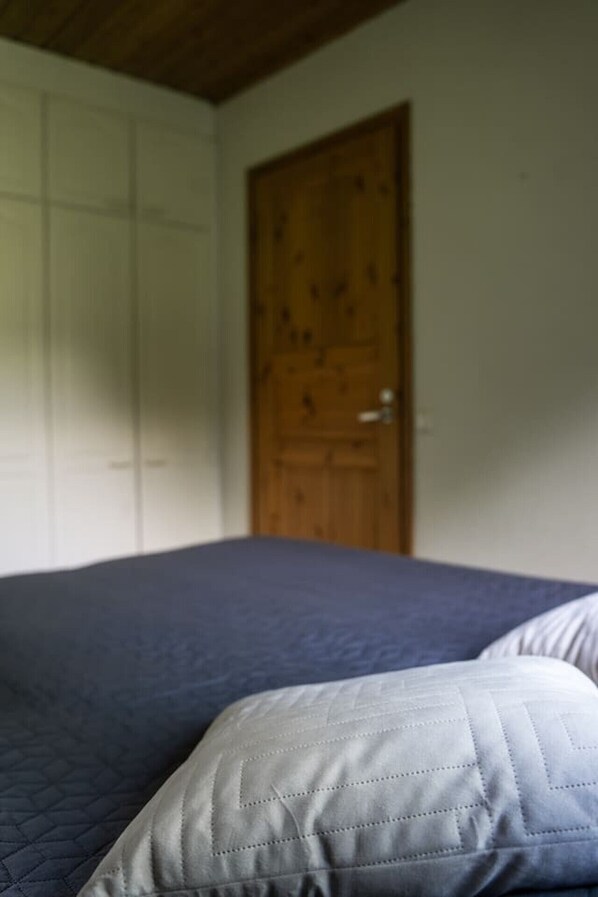 Un dormitorio con una cama, una puerta de madera y una pared blanca.