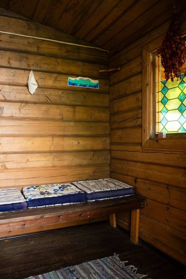 Interior de una cabaña de madera con un banco, un letrero pequeño en la pared y una ventana con diseño de vitral.