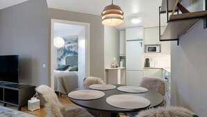 Ein modernes Wohnzimmer mit einem runden Esstisch, kuscheligen Sesseln, einem Flachbildfernseher und einer Küchenzeile mit Mikrowelle.