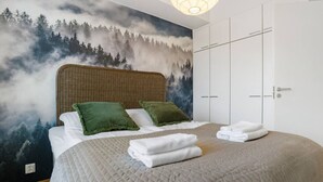 Ein Schlafzimmer mit einem Bett, grünen Kissen, einer gesteppten Bettdecke und einem Wandgemälde von einem Wald.