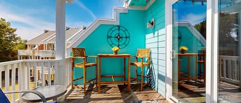A covered outdoor deck with a wooden table and chairs, a compass wall decoration, and a view of neighboring houses.