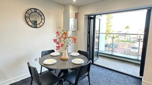 A dining area with a round table, black chairs, a clock, and a vase with flowers. - Bright Spacious Apartment Featuring Large Balcony and Free Parking (Marston)