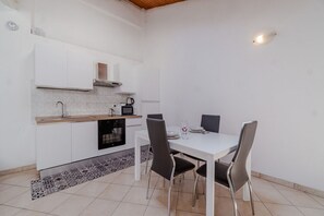 A compact kitchen with white cabinets, a microwave, a stove, and a dining table with four chairs.