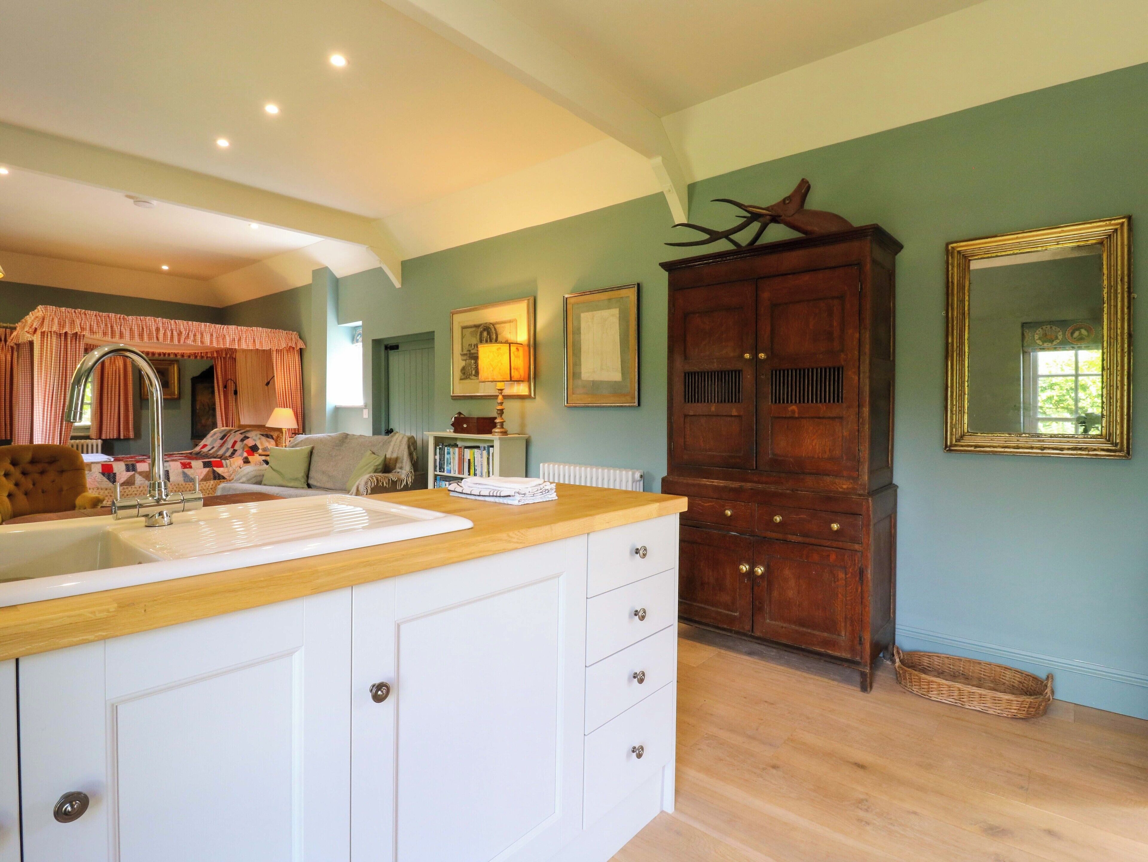 A kitchen with a wooden countertop, white cabinets, a sink, and a large mirror.