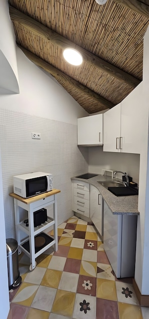 Una cucina compatta con un forno a microonde su un ripiano, un lavello, pensili e un pavimento a fantasia.