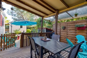Une terrasse couverte avec une table et des chaises, une clôture en bois et des plantes en pot.