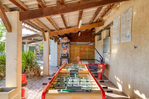 Una mesa de fútbol de mesa bajo una pérgola de madera, con un letrero colgado en la pared y un tablón de anuncios.