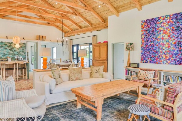 A spacious living area with a wooden ceiling, a large sofa, a coffee table, and a bookshelf.