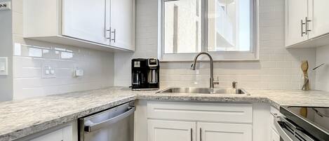 A modern kitchen with white cabinets, a stainless steel dishwasher, and a coffee maker.