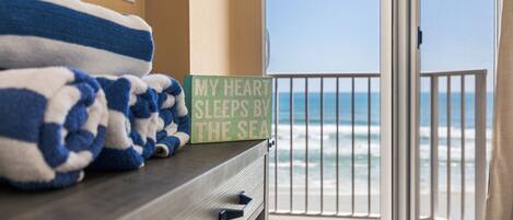 A room with a view of the sea, a sign reading "My heart sleeps by the sea," and a stack of blue and white towels on a wooden dresser.