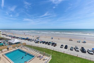 Vista de una playa con piscina, sombrillas y coches estacionados.