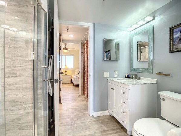 Un baño moderno con cabina de ducha de vidrio, tocador blanco con encimera de mármol y un inodoro.