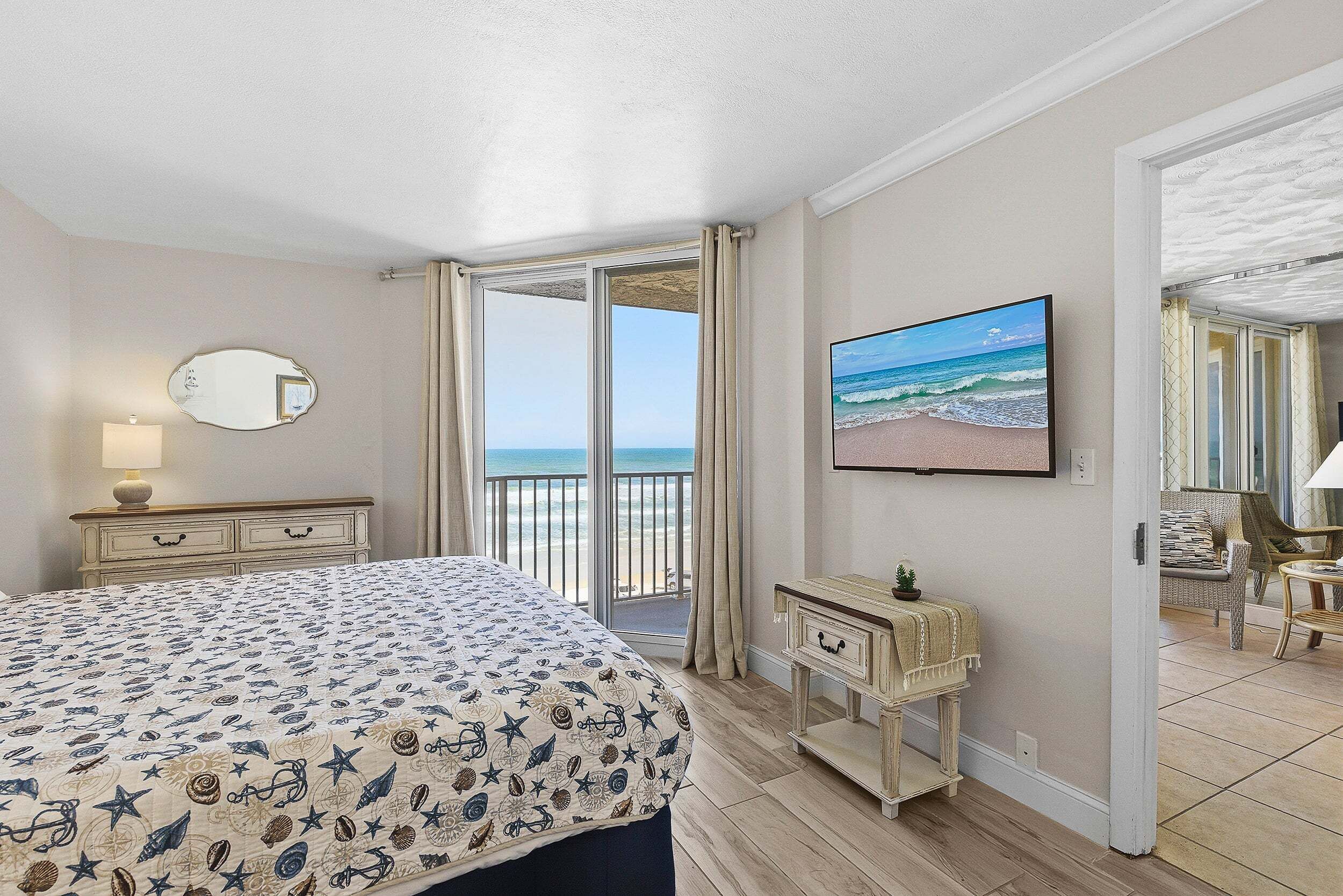 Un dormitorio con cama, cómoda, espejo, un cuadro y balcón con vista al océano.
