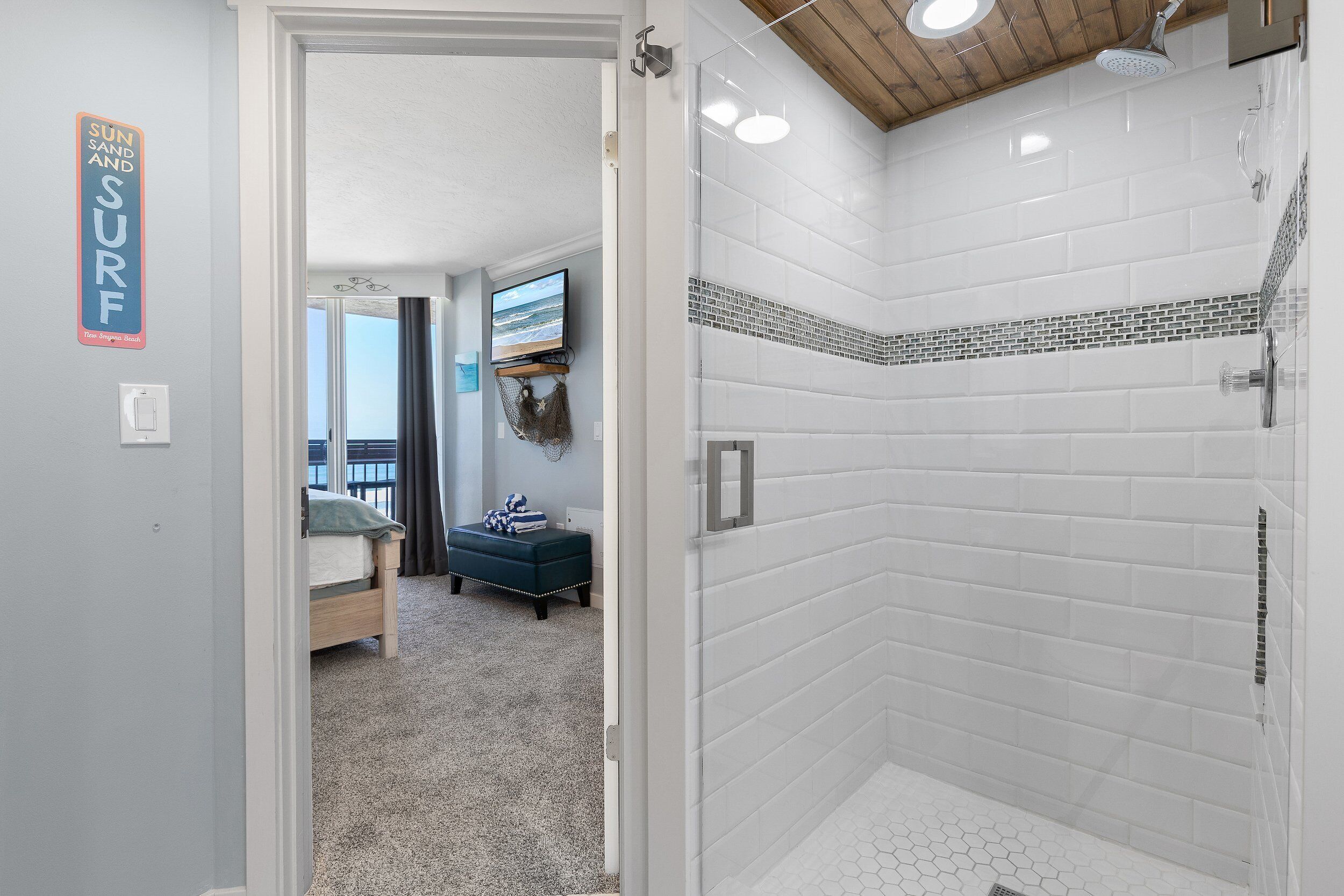 A bathroom with white subway tiles, a shower, and a toilet. There is a sign on the wall that says "SUN AND SURF".