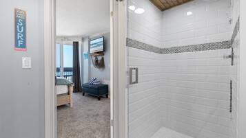A bathroom with white subway tiles, a shower, and a toilet. There is a sign on the wall that says "SUN AND SURF".