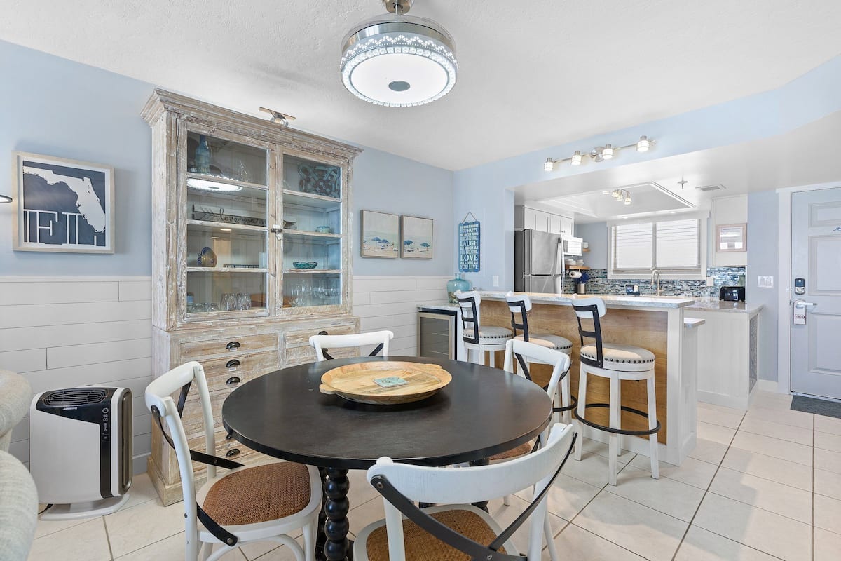 Un coin repas avec une table ronde, des chaises blanches, un buffet aux portes vitrées et, au fond, une cuisine.