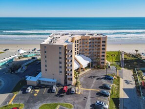 A beachfront hotel with multiple floors, a parking lot, and a view of the ocean.