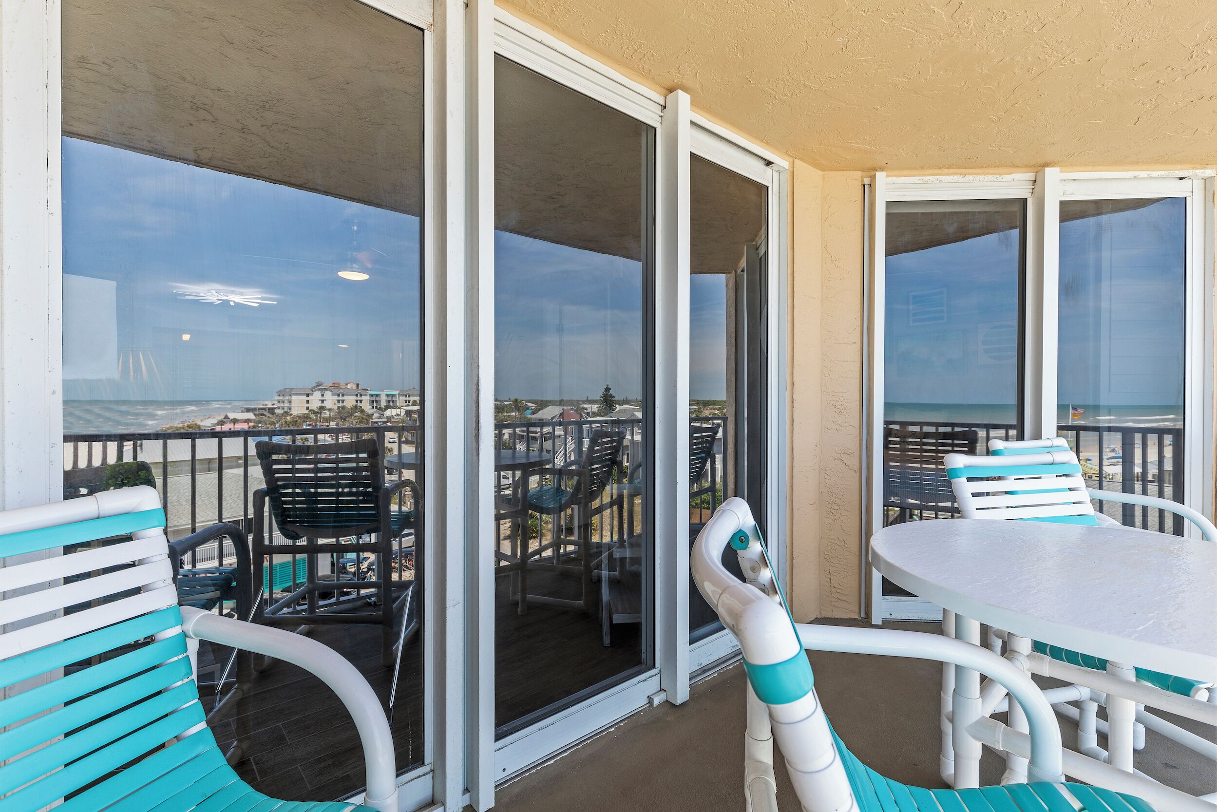 A balcony with a table and chairs, a view of the beach, and a building in the distance.