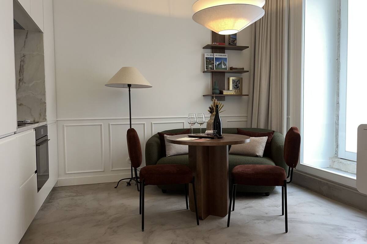 A dining area with a round table, two chairs, a lamp, and a green sofa.
