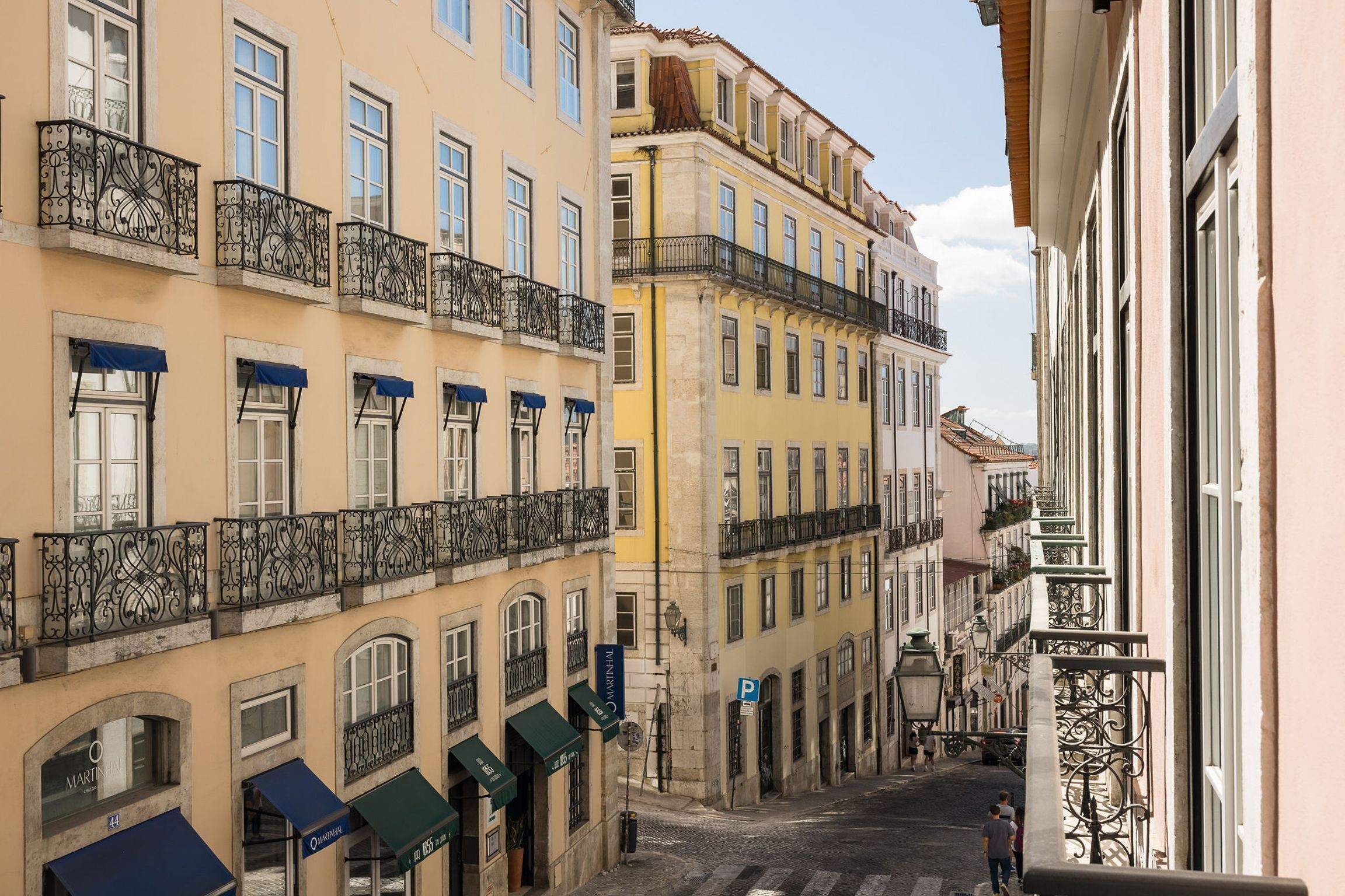 A narrow street lined with multi-story buildings, featuring balconies with wrought iron railings and awnings over the windows.