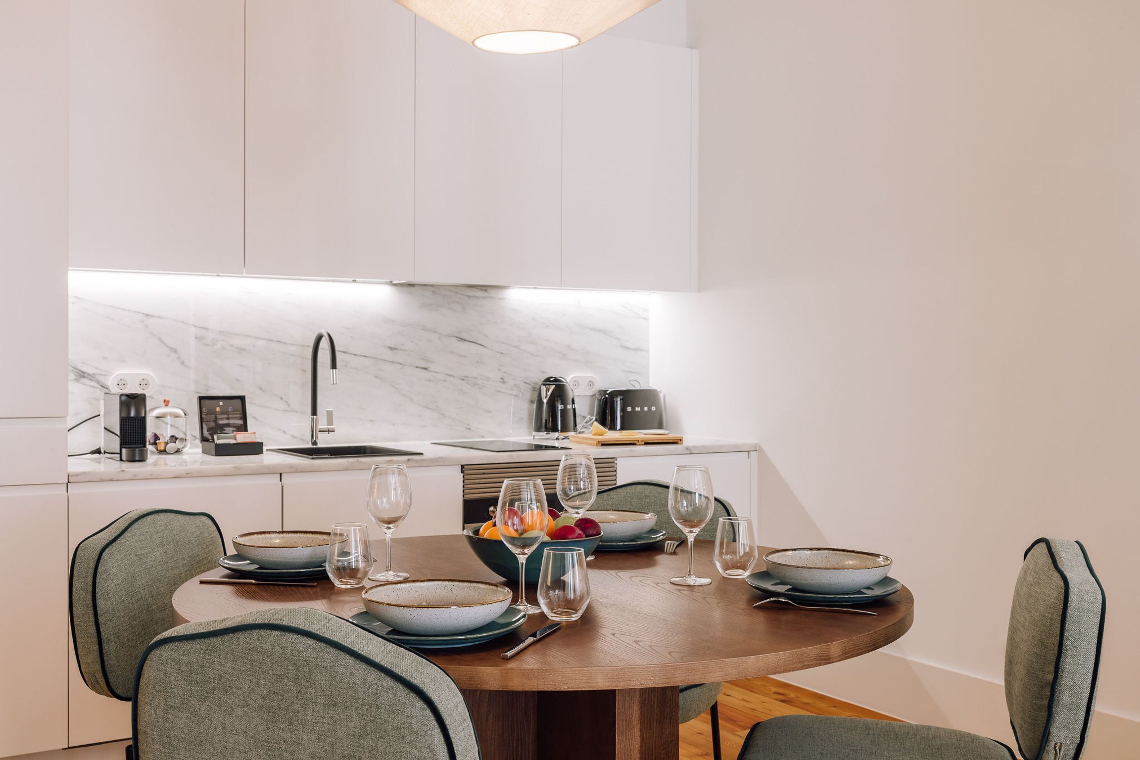 Una cocina moderna con encimera de mármol, una mesa de comedor dispuesta con platos, vasos y un frutero.