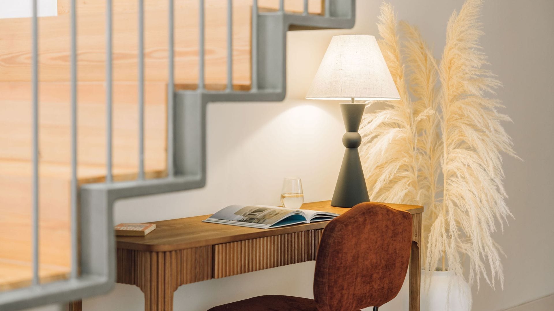 A wooden desk with a lamp, a glass of water, and a book.