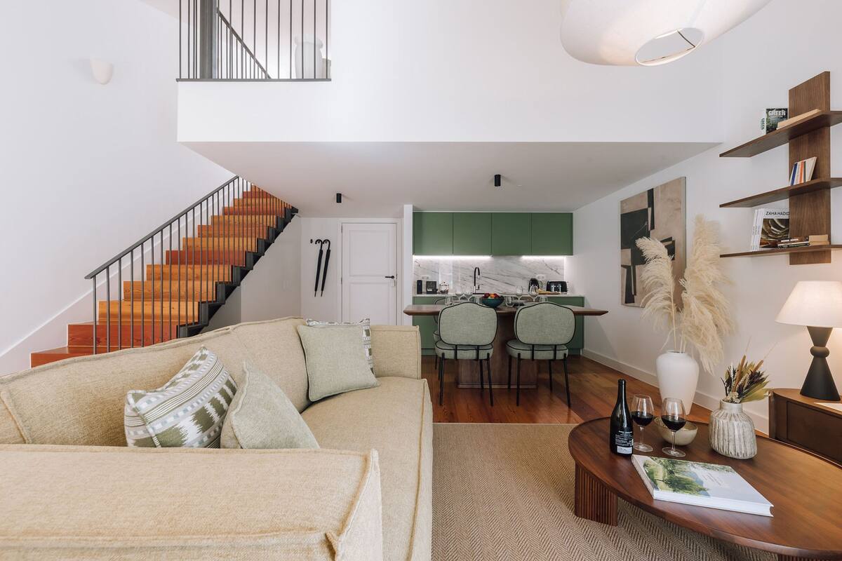 A modern living room with a sofa, a coffee table with a magazine, and a dining area with chairs and a kitchen in the background.