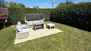 A backyard with a patio set, a white dog, and a hedge.