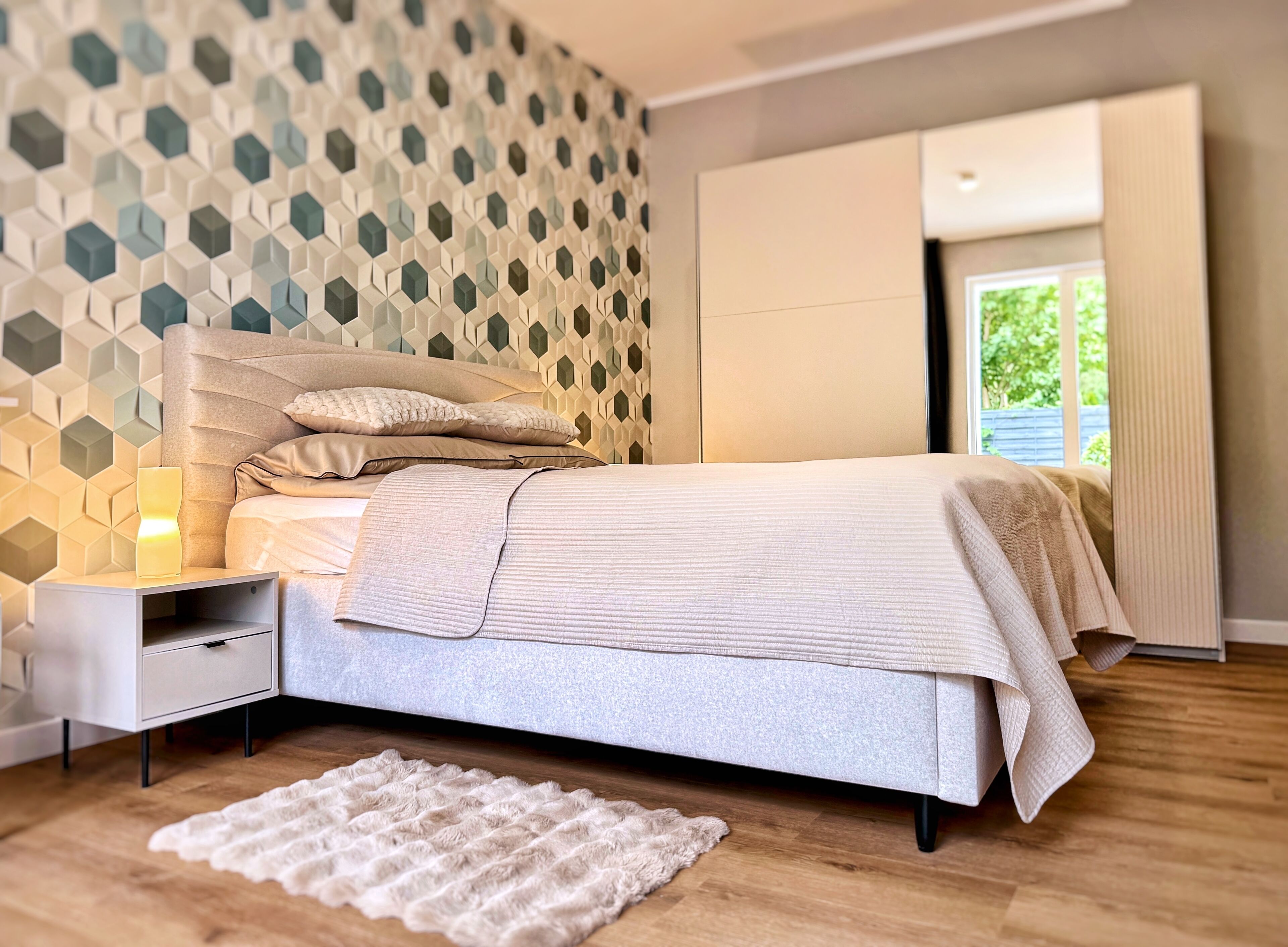 Un dormitorio con cama, mesita de noche y pared con un diseño geométrico.