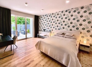 A bedroom with a large bed, a desk, and a chair, a sliding glass door to a patio, and a geometric patterned wall. - Modern Villa & Private Garden - Fully Renovated 2025 🏡 (Warszawa)