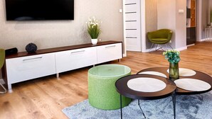 A modern living room with a flat-screen TV, a white cabinet, a green ottoman, a round coffee table, and a blue rug. - Modern Villa & Private Garden - Fully Renovated 2025 🏡 (Warszawa)