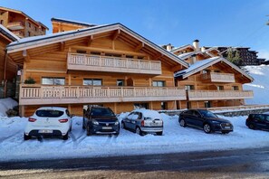 A wooden chalet-style building with multiple balconies and a ski slope in the background.