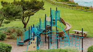 A playground with a slide, climbing structures, and a picnic table. - Panoramic Loft with King Bed & Full Kitchen (Otter Rock)