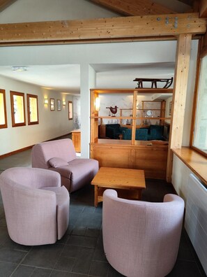 Un interior acogedor con techo de madera, una zona de estar con dos sofás y una mesa, y vistas a una cocina con un banco de madera y una escultura de pájaro.