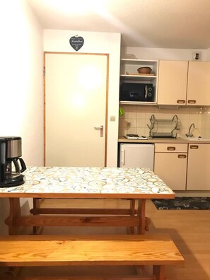 Cozinha compacta com mesa, banco, micro-ondas e armários.