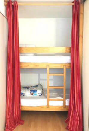 Uma cama beliche com escada, cortinas vermelhas e um colchão branco.